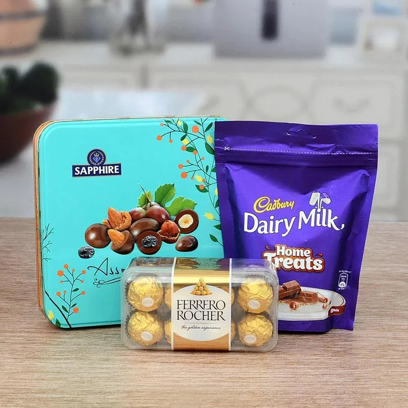 Sapphire chocolate tin, Cadbury Dairy Milk Home Treats, and Ferrero Rocher on a wooden surface.