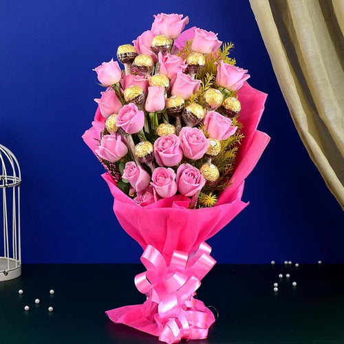 Bouquet of pink roses with chocolate candies wrapped in pink paper on a dark surface.
