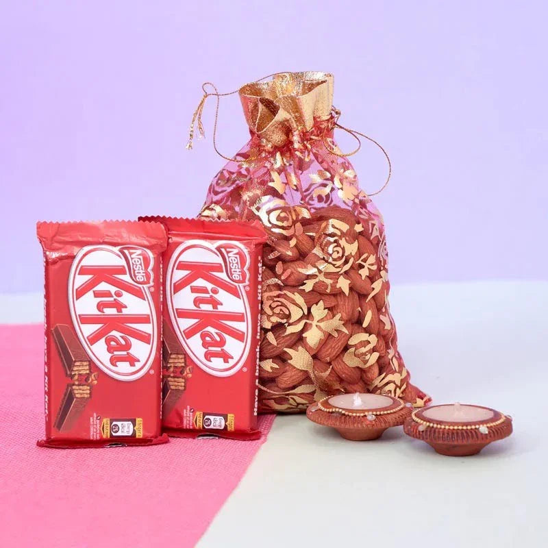 Two Kit Kat chocolate bars with a decorative gold bag and two small clay lamps on a pink and white background.