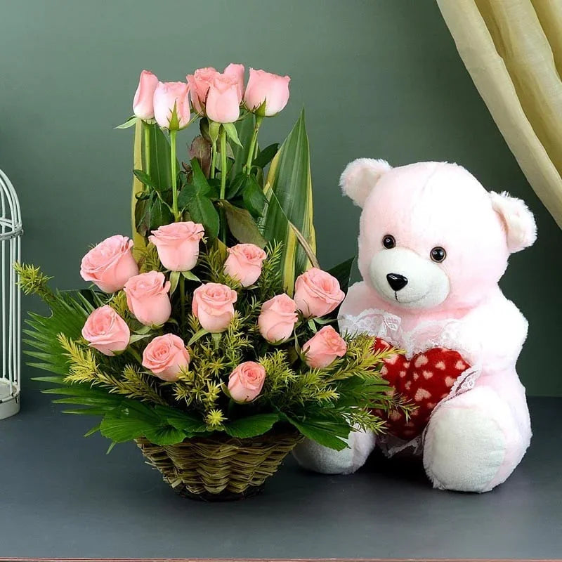 Basket of pink roses and a white teddy bear with a red heart on a dark surface.