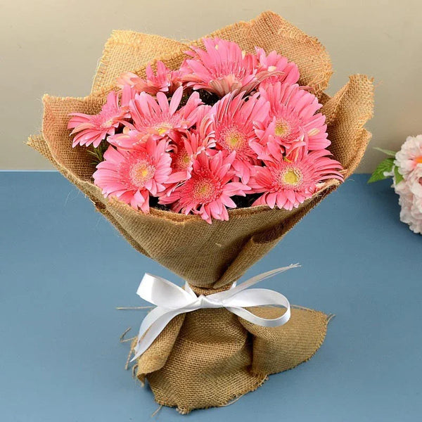Bouquet of pink flowers wrapped in brown paper with a white ribbon on a blue surface.