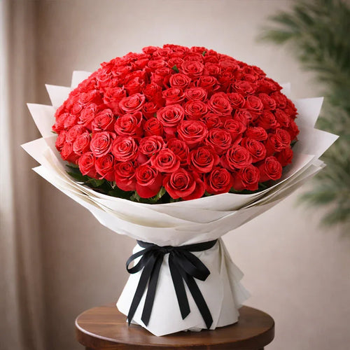Bouquet of red roses wrapped in white paper with a black ribbon on a wooden table.
