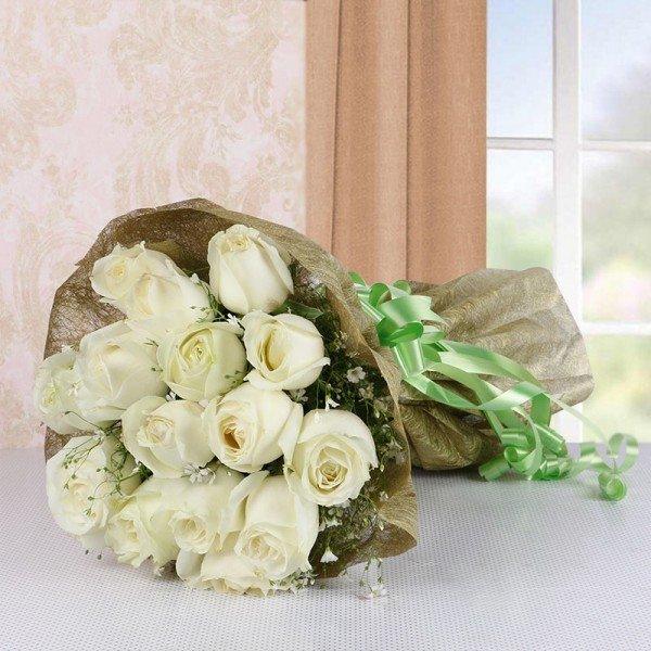 Bouquet of white roses wrapped in brown paper with a green ribbon on a light surface.