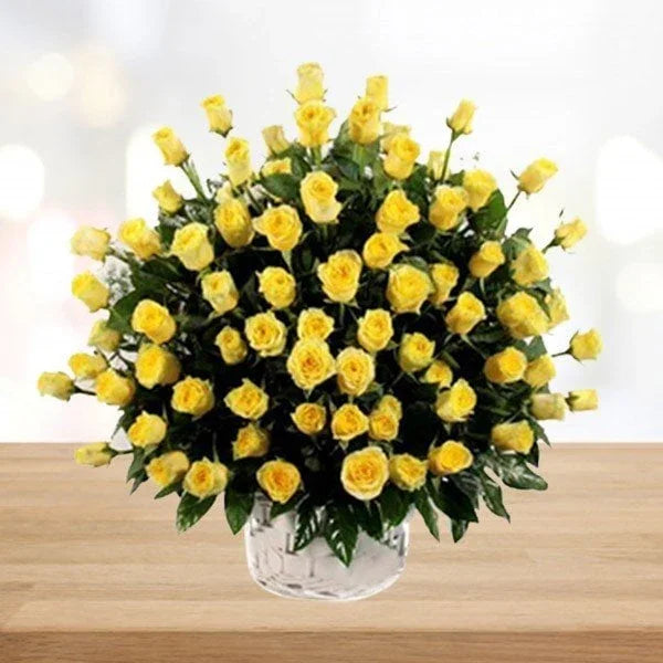 Bouquet of yellow roses in a clear vase on a wooden surface with a blurred background