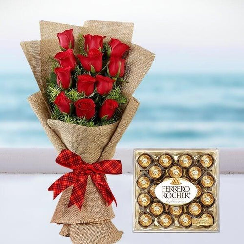 Bouquet of red roses wrapped in burlap with a red ribbon, next to a box of Ferrero Rocher chocolates, against 
