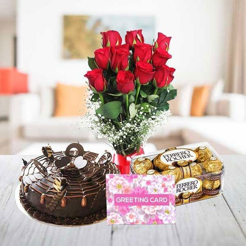 Chocolate cake, bouquet of red roses, Ferrero Rocher chocolates, and a greeting card on a table.