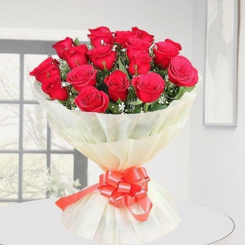 Bouquet of red roses wrapped in cellophane with a red ribbon on a light background