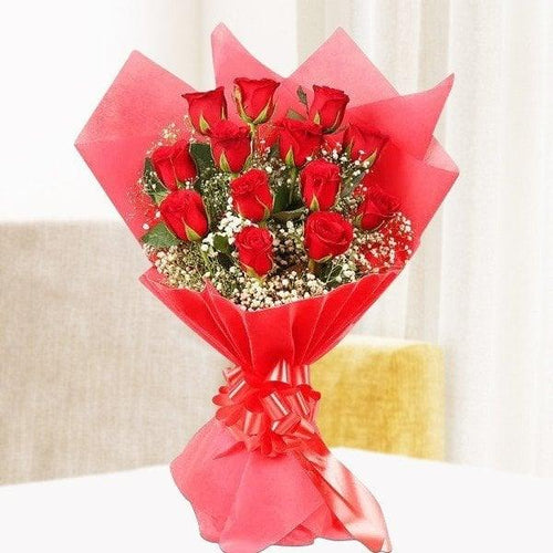 Bouquet of red roses wrapped in red paper on a white surface 