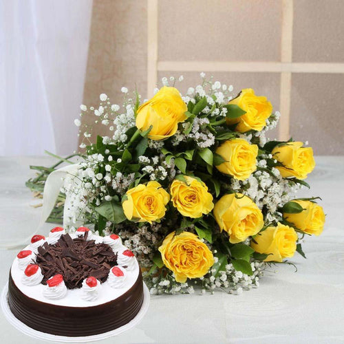 Chocolate cake with white frosting and red berries, accompanied by a bouquet of yellow roses on a light background.