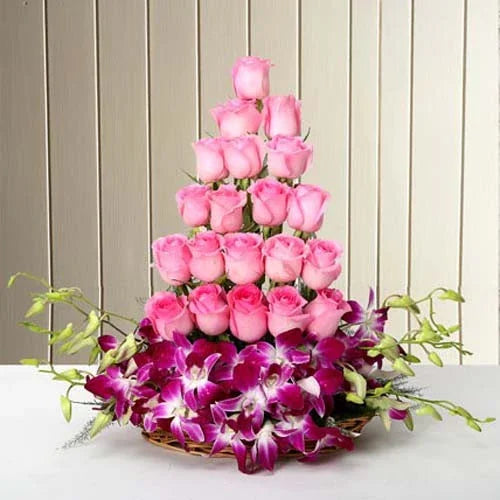 Pink roses arranged in a tiered bouquet with purple orchids in a woven basket