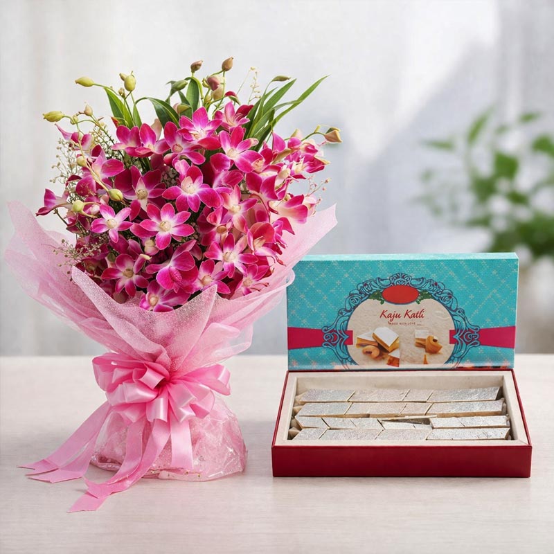 Bouquet of pink flowers with a box of Kaju Katli on a white surface.