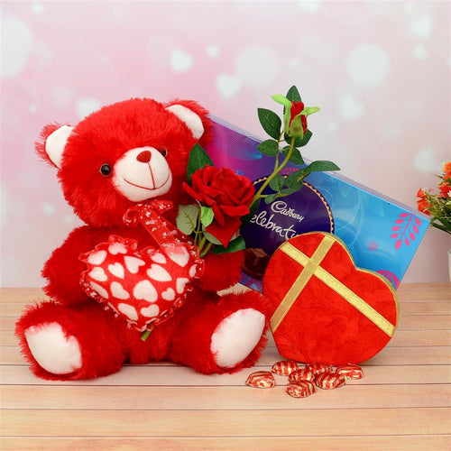 Red teddy bear with a bouquet of roses, heart-shaped box, and Cadbury chocolate on a wooden surface.