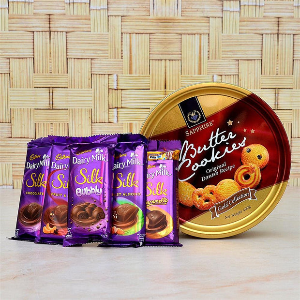 Assorted chocolate bars and a tin of cookies on a wooden surface with a woven background