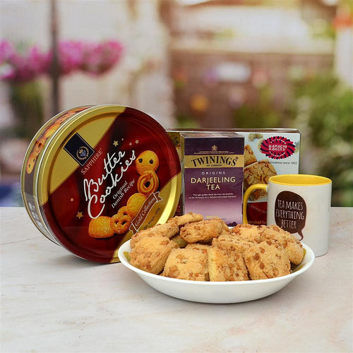 Butter cookies in a tin, a mug, and a box of Twinings Darjeeling tea on a table.