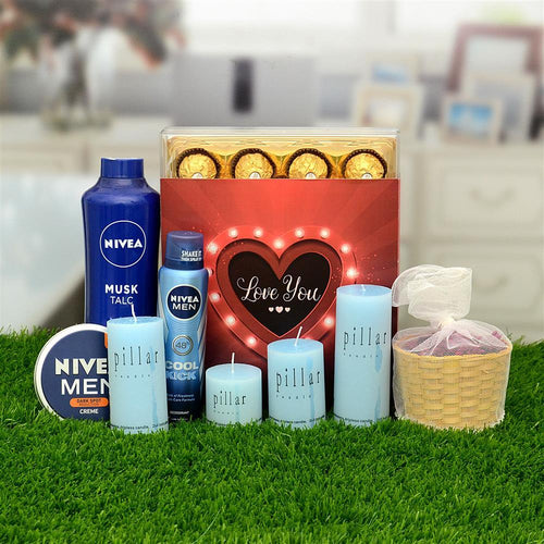 Gifting arrangement with Nivea products, candles, and a heart-shaped 'Love You' box on grass.