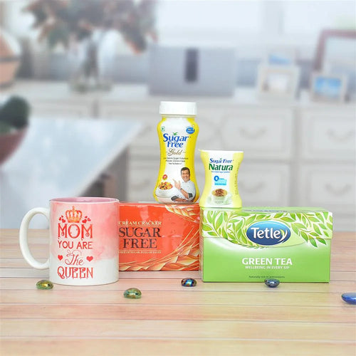 Mug with 'Mom you are the queen' text, boxes of sugar-free products, and Tetley green tea on a table.