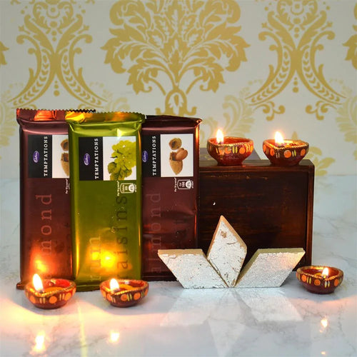 Three packets of Temptations Chocolate treats with lit Diya and decorative items on a patterned background