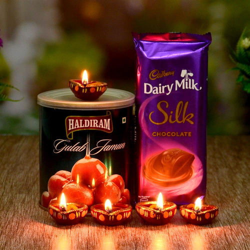 Haldiram Gulab Jamun can and Cadbury Dairy Milk Silk chocolate bar with lit Diwali Diya 