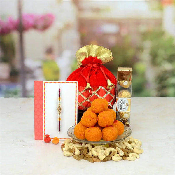 Decorative arrangement with laddus, cashews, a red and gold gift bag, and Rakhi on a white surface.