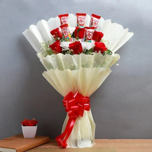 Bouquet of red roses and KitKat chocolate bars wrapped in white paper with a red bow on a gray background.
