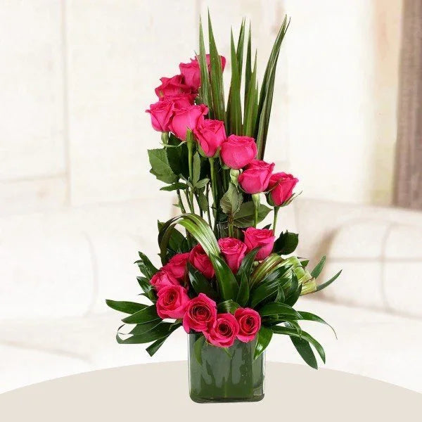 Bouquet of pink roses with green leaves in a clear vase on a white surface.