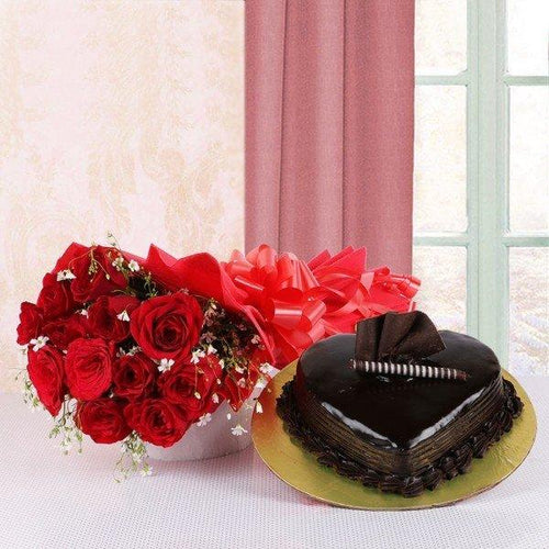Bouquet of red roses with a red bow and a chocolate cake on a white table.