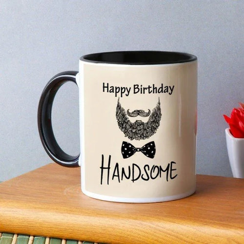 Beige mug with black interior and handle, featuring a beard, mustache, bow tie, and 'Happy Birthday Handsome' text on a wooden surface.