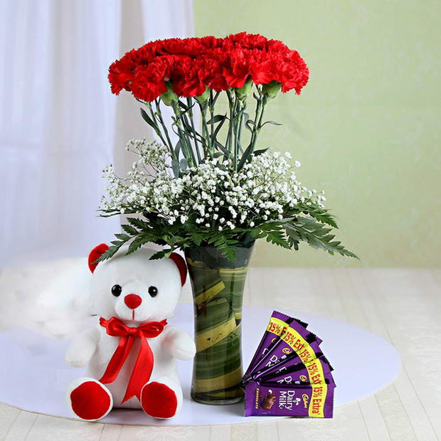 Bouquet of red flowers with a white teddy bear and purple packets on a light surface.
