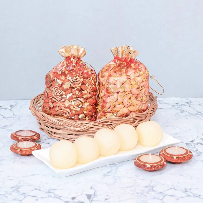 Two decorative bags with floral patterns in a basket, surrounded by white spherical objects and small red candles on a marble surface.