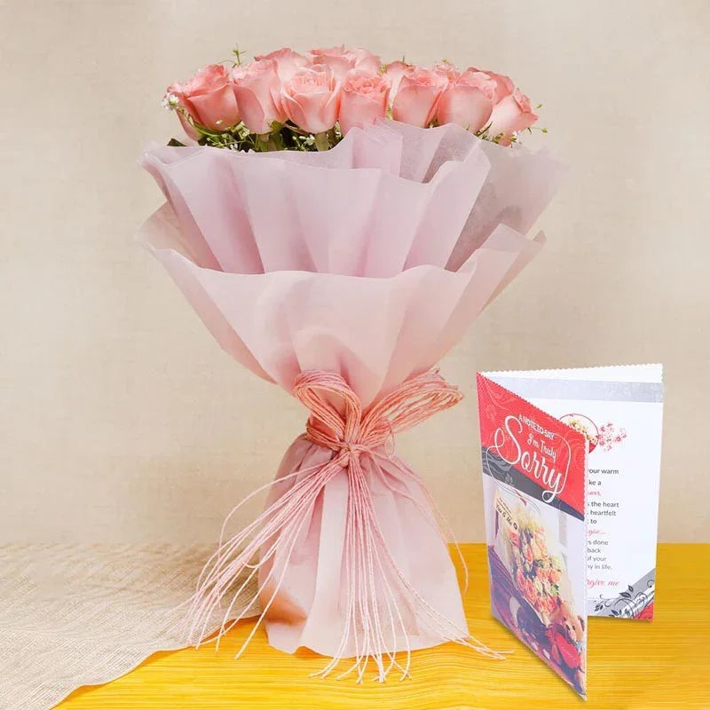 Bouquet of pink roses wrapped in pink paper with a 'Sorry' card on a yellow surface.