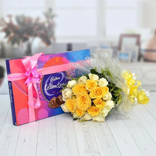 Bouquet of yellow and white roses with a Cadbury Celebrations chocolate bar on a wooden surface.