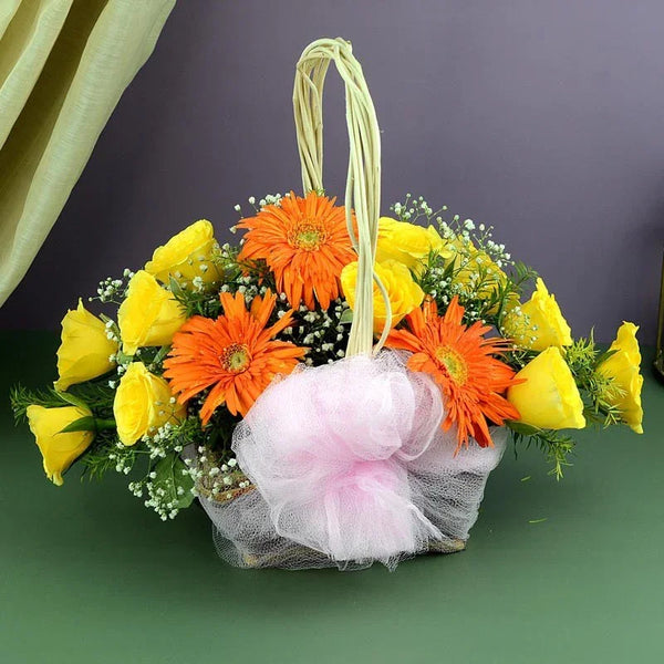 Floral arrangement in a basket with yellow and orange flowers on a green surface.