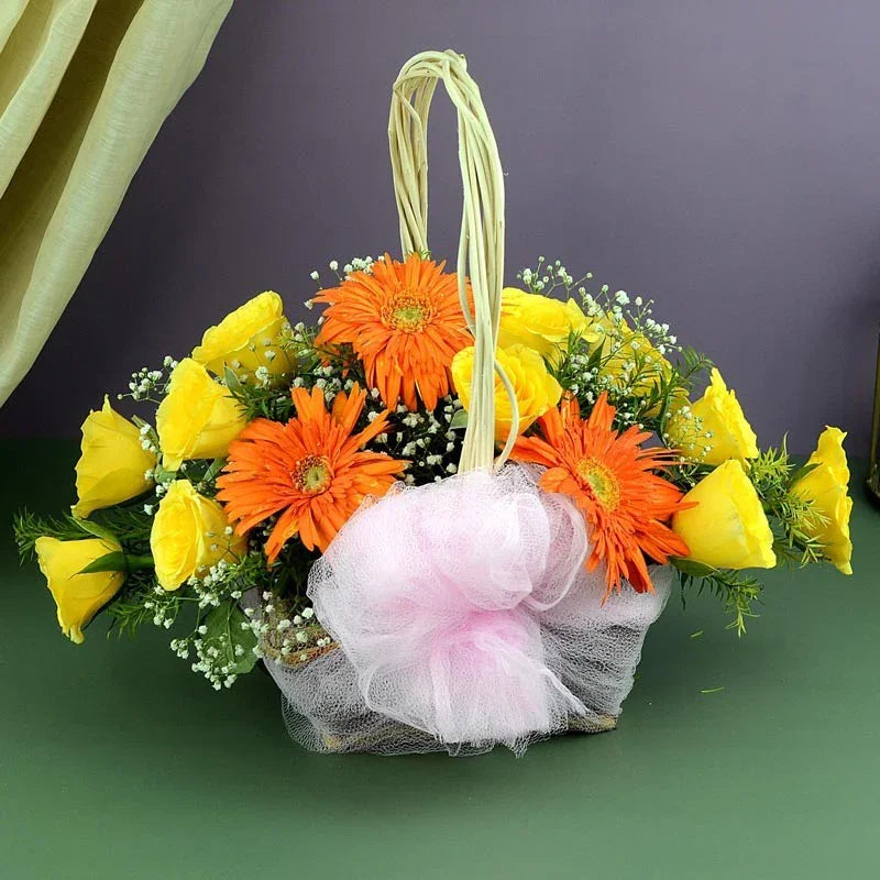Floral arrangement in a basket with yellow and orange flowers on a green surface.