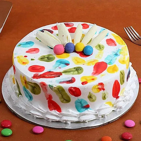 Colorful Holi-themed pineapple cake with white frosting, rainbow splashes, and candy decor