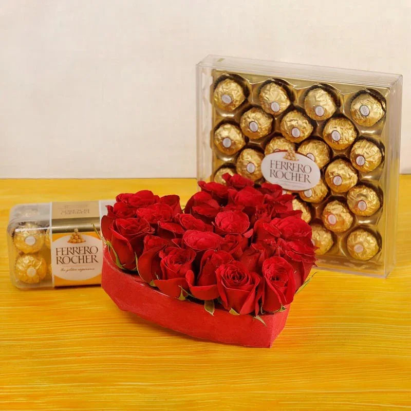 Heart-shaped arrangement of red roses with a box of Ferrero Rocher chocolates on a yellow surface.