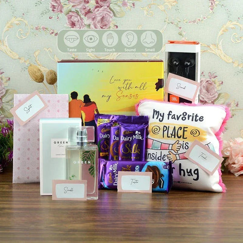 Collection of gifts including a perfume bottle, chocolate bars, and a pillow with text on a decorative background.