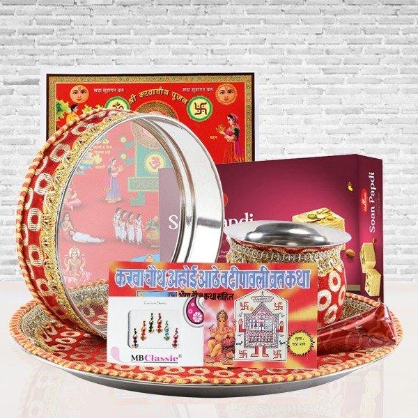 Decorative karva chauth items including a tray, bowls, and a box on a white brick wall background