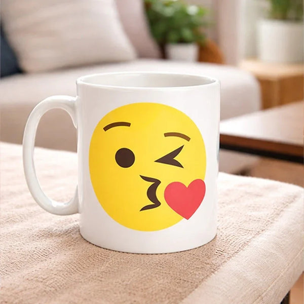 White ceramic mug with a yellow kiss emoji and red heart, on a cozy indoor table.