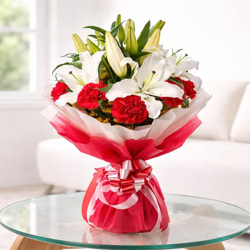 Bouquet of flowers wrapped in red paper with a bow on a glass table.
