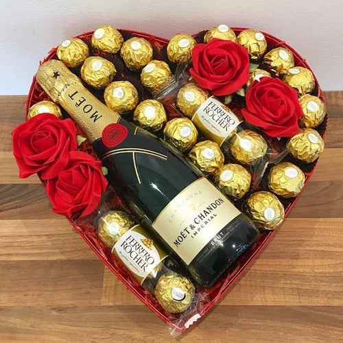 Heart-shaped arrangement of red roses, Ferrero Rocher chocolates, and Moët & Chandon champagne on a wooden surface.