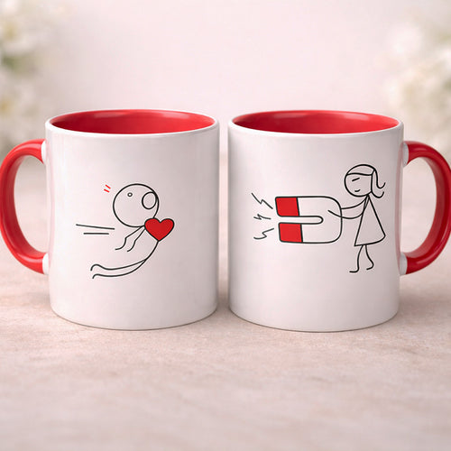 Two mugs with red interior and handles, featuring stick figure drawings of a couple exchanging a heart.