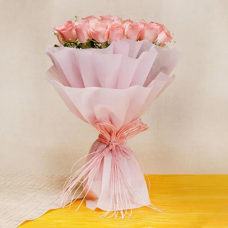 Bouquet of pink roses wrapped in pink tissue paper on a yellow surface with a beige background