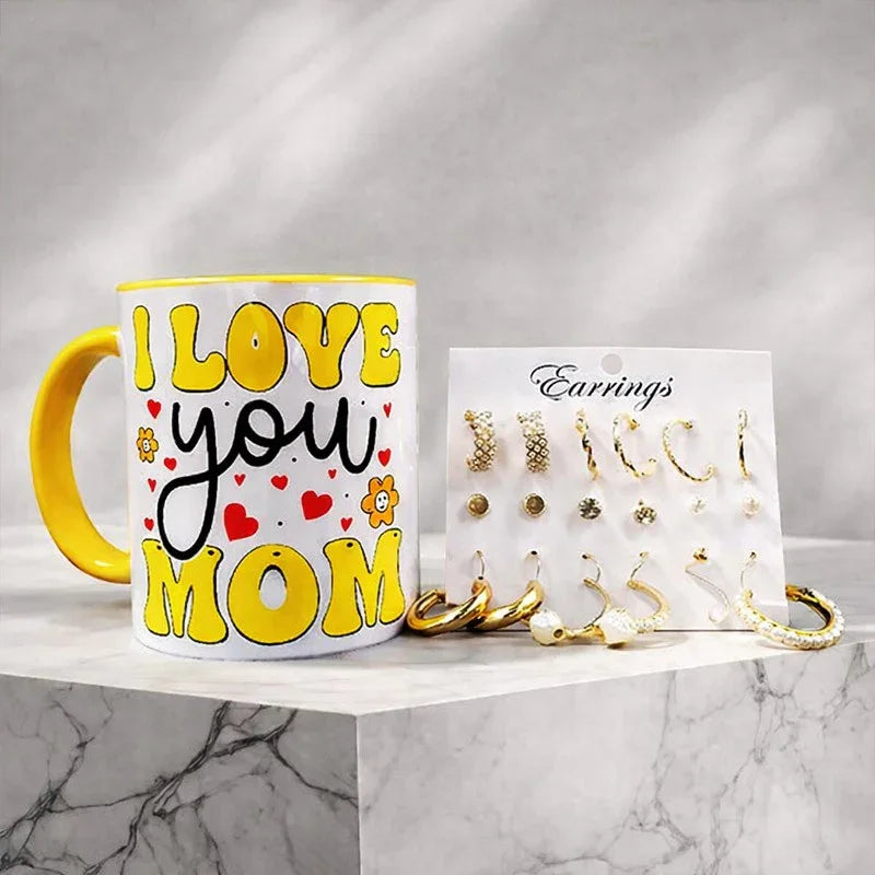Mug with 'I Love You Mom' text and a display of earrings on a marble surface.