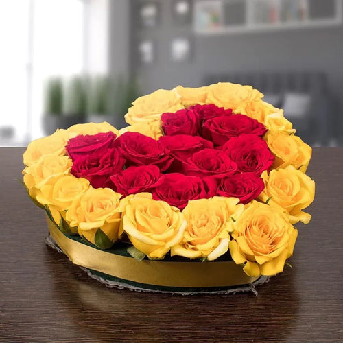 Heart-shaped arrangement of red and yellow roses on a wooden table.