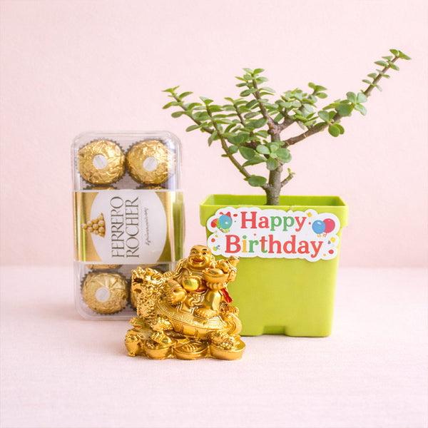 Gold statue, Ferrero Rocher chocolates, and a potted plant with a 'Happy Birthday' sign on a pink background