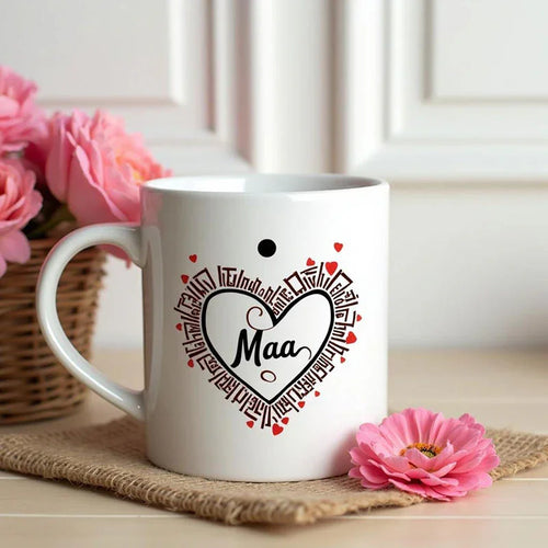 White mug with 'Maa' design on a wooden surface with pink flowers