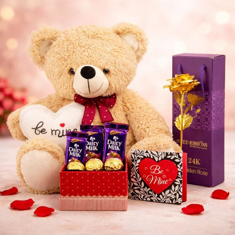 Teddy bear with 'be mine' heart, Dairy Milk chocolate, and gold rose on a soft pink background