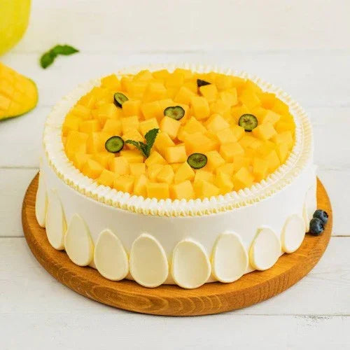 Round mango cake topped with fresh mango cubes and berries on a wooden board