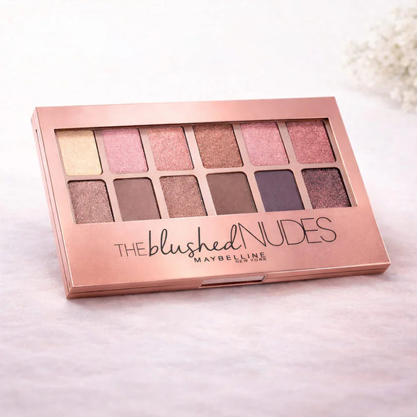 Eyeshadow palette with 12 nude and pink shades in a rose gold case on a light background.