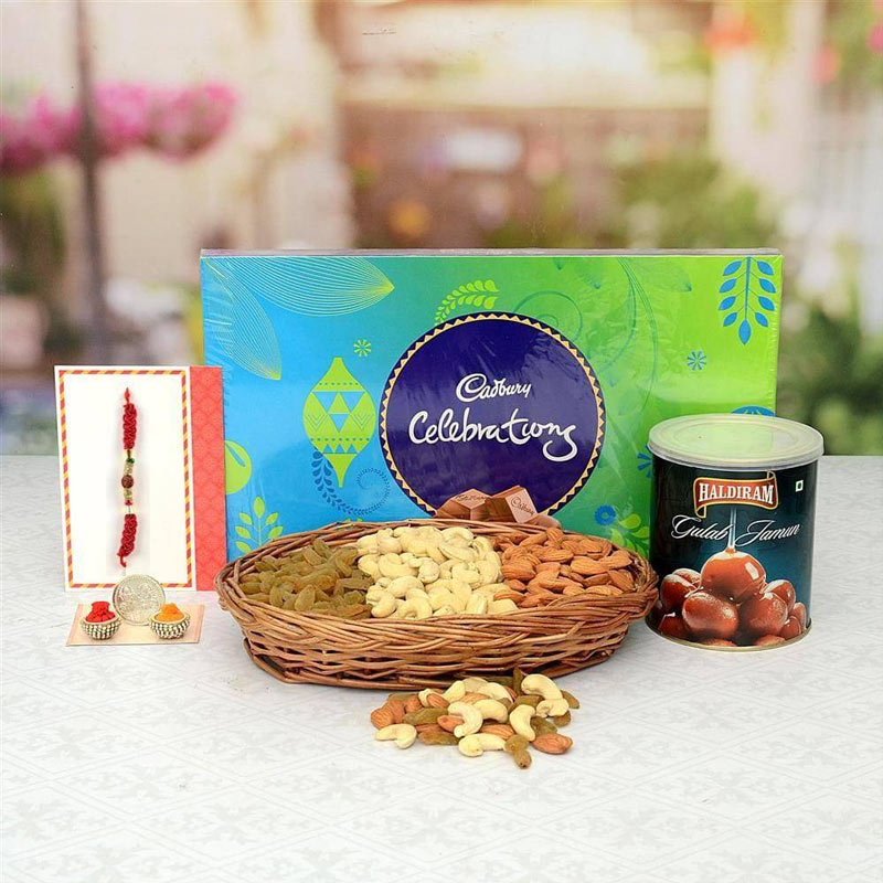 Assorted dry fruits, Cadbury Celebrations chocolate box, and Haldiram sweet can on a white surface with blurred greenery in the background.